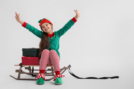 Little girl with sled and Christmas gifts on light backgroundの写真素材