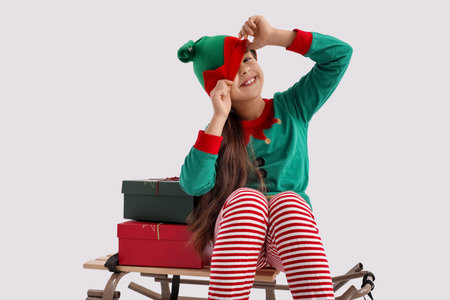 Little girl with sled and Christmas gifts on light background