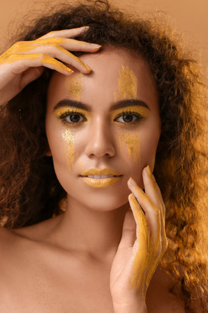 Beautiful young woman with yellow paint on her face and body against color background