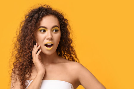 Beautiful African-American woman with makeup in yellow tones on color backgroundの写真素材