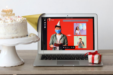Laptop, gift and cake on table in room. Celebrating birthday online due to coronavirus epidemicの写真素材
