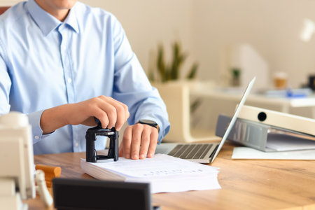 Young male notary public attaching seal to documents in officeの写真素材