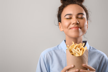 Young African-American woman with french fries on light backgroundの写真素材
