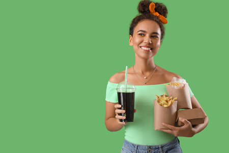 Young African-American woman with french fries and cola on green backgroundの写真素材