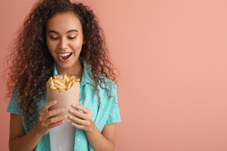 Happy African-American woman with french fries on color backgroundの写真素材