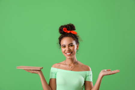 Beautiful young African-American woman with book on green backgroundの写真素材