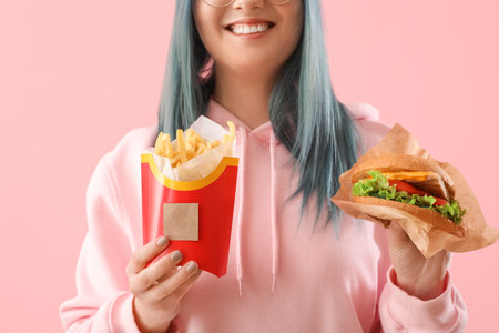 Young woman with unusual hair holding burger and french fries on color backgroundの写真素材