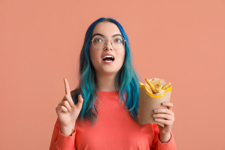 Young woman with unusual hair and french fries having idea on color backgroundの写真素材