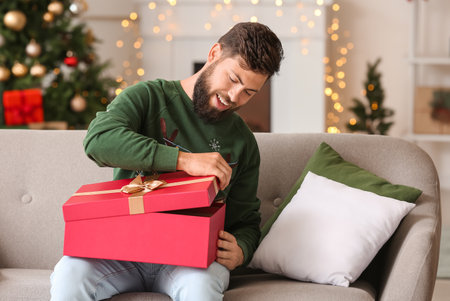 Happy man opening Christmas gift at homeの写真素材