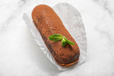 Delicious chocolate eclair on light background
