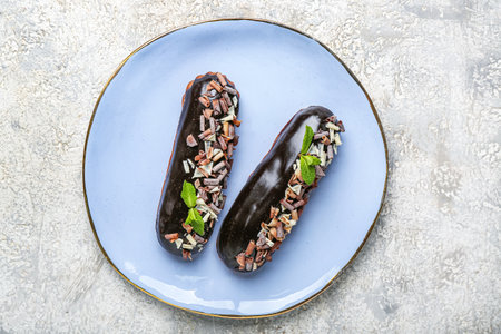 Plate with tasty chocolate eclairs on light background