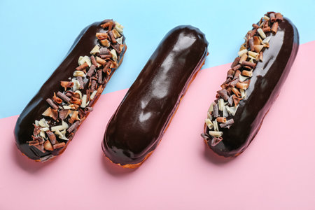 Tasty chocolate eclairs on color background
