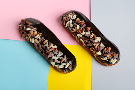 Delicious chocolate eclairs on color background