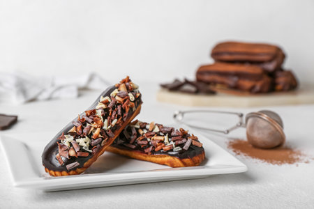 Plate with tasty chocolate eclairs on light tableの写真素材