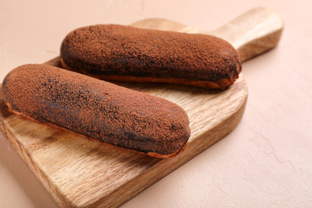 Wooden board with delicious chocolate eclairs on color background, closeup