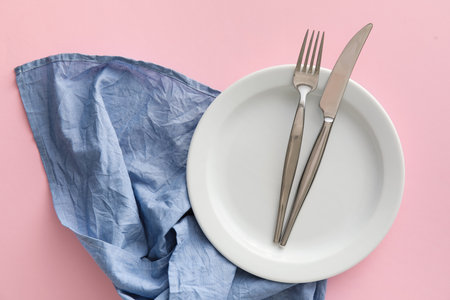 Table setting with cutlery in plate and blue napkin on pink backgroundの写真素材
