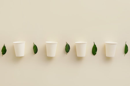 Row of paper cups and plant leaves on white backgroundの写真素材