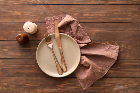 Table setting with cutlery in plate, napkin, salt and pepper shakers on wooden backgroundの写真素材