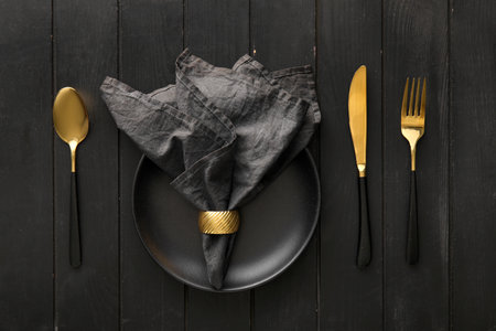 Stylish table setting with napkin in plate and cutlery on black wooden backgroundの写真素材