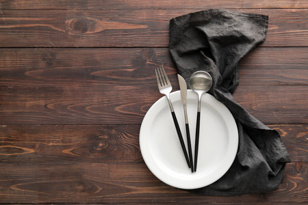 Table setting with cutlery in plate and black napkin on wooden backgroundの写真素材