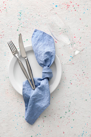 Simple table setting with cutlery, napkin in plate and glass on light background