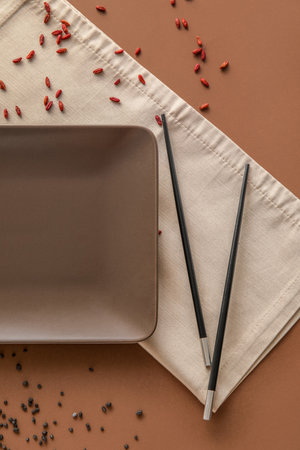 Table setting with chopsticks and scattered seeds on brown background