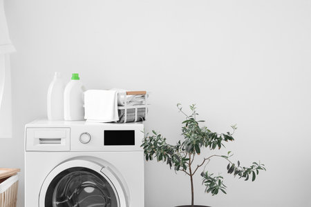Basket with towels and bottles of detergent on washing machine near light wallの写真素材