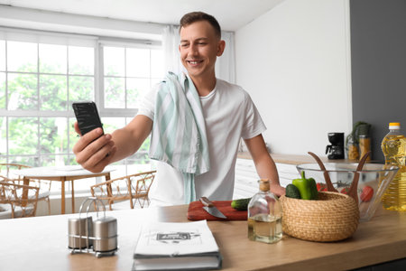 Young man with mobile phone taking selfie in the kitchenの写真素材