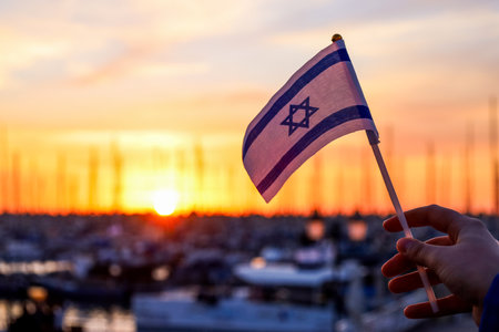 Female hand holding flag of Israel against sunset sky background