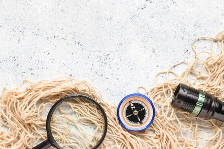 Magnifier, compass, flashlight and fishnet on light background