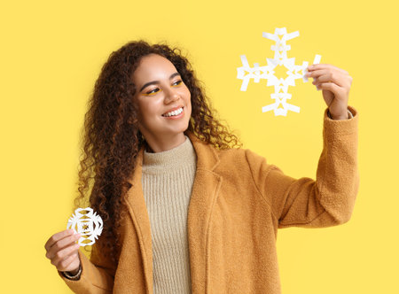 Beautiful African-American woman with paper snowflakes on yellow backgroundの写真素材