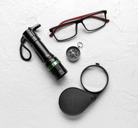 Eyeglasses, compass, magnifier and flashlight on light background