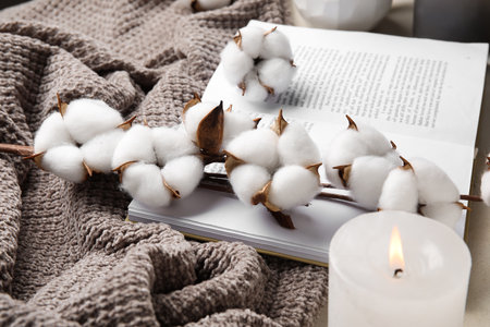 Burning candle, opened book, cotton flowers and fabric on tableの写真素材