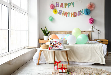 Laptop and gifts in the interior of the bedroom. Celebrating birthday online due to coronavirus epidemicの写真素材