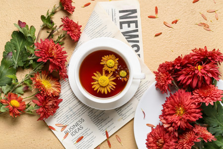 Composition with cup of tea, newspaper and chrysanthemum flowers on color background, closeup