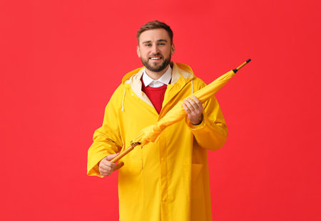 Young man in stylish raincoat and umbrella on color backgroundの写真素材