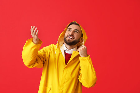Young man in stylish raincoat showing something on color backgroundの写真素材