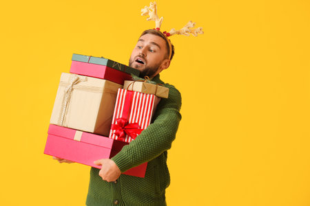 Young man with many Christmas gifts on color backgroundの写真素材