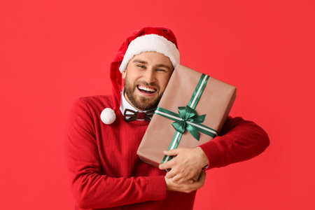 Happy young man with Christmas gift on color backgroundの写真素材