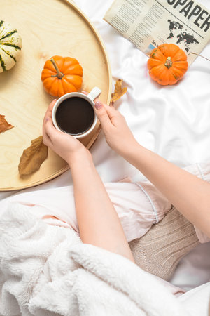 Woman drinking tasty pumpkin coffee on bedの写真素材