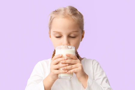 Cute little girl drinking milk on lilac backgroundの写真素材
