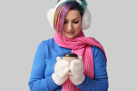 Extravagant woman in winter clothes and with coffee on gray background