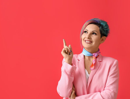Beautiful woman with unusual hair pointing at something on color backgroundの写真素材