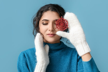 Beautiful woman with closed eyes holding red snowflake near face on blue backgroundの写真素材