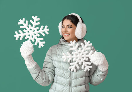 Beautiful smiling woman in warm clothes holding big snowflakes on green background