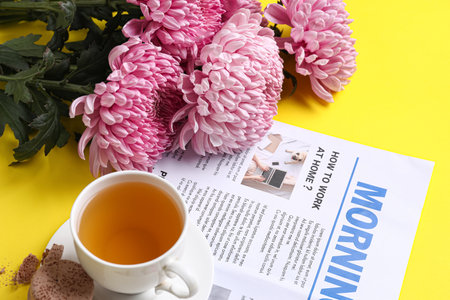 Beautiful chrysanthemum flowers, newspaper and cup of tea on yellow background, closeupの写真素材
