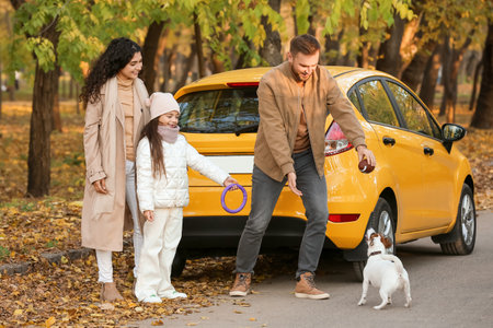 Happy family playing with cute dog near yellow car on autumn dayの写真素材