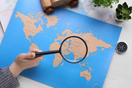 Woman holding magnifying glass above map on light background