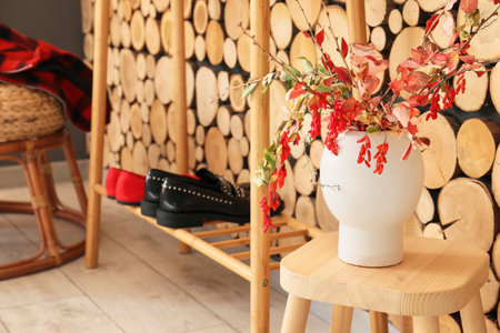Vase with autumn branches on chair in room