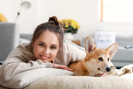 Young woman with cute Corgi dog lying on pouf at homeの写真素材